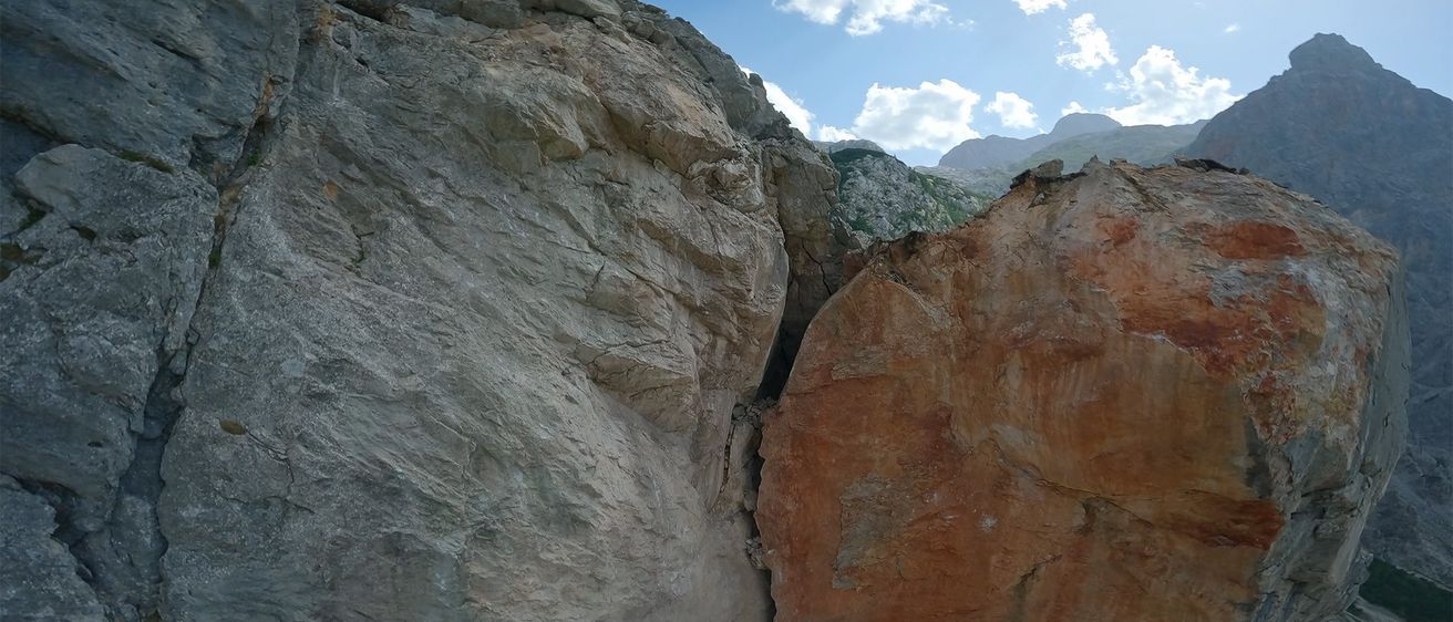 Eine felsige Klippe mit einer tiefen Schlucht und den Worten 'COPTER COOPERATION' darüber. Der Himmel ist blau mit verstreuten Wolken und fernen Bergen.