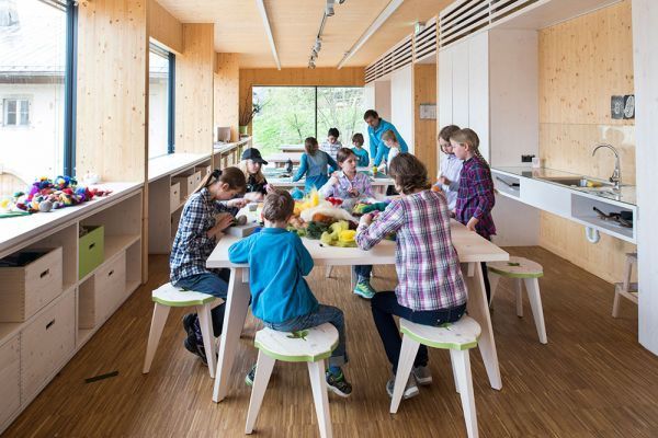 Mehrere Kinder sitzen um einen Tisch in einem Raum mit Holzböden und -wänden und beschäftigen sich mit einer Bastelaktivität.