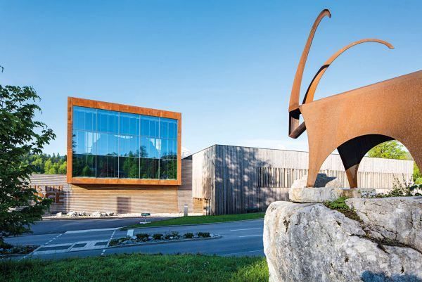 Ein modernes Gebäude mit Glasfassaden und einer großen braunen Metallskulptur davor.