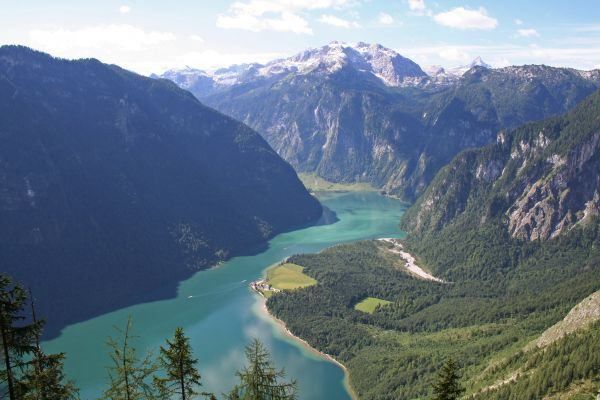 Ein atemberaubender Blick von oben auf einen friedlichen See, der zwischen hohen Bergen eingebettet ist, mit üppigem Grün und einem klaren blauen Himmel.