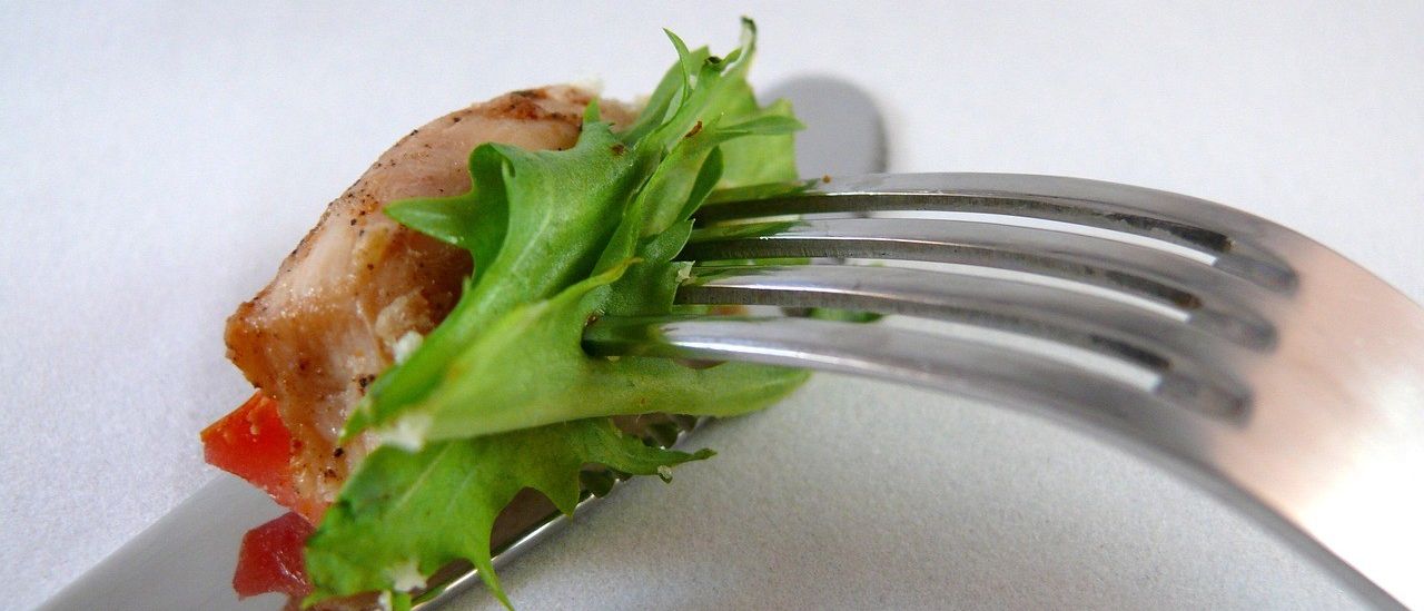 Close-up of a piece of chicken and arugula on a fork against a white background.
