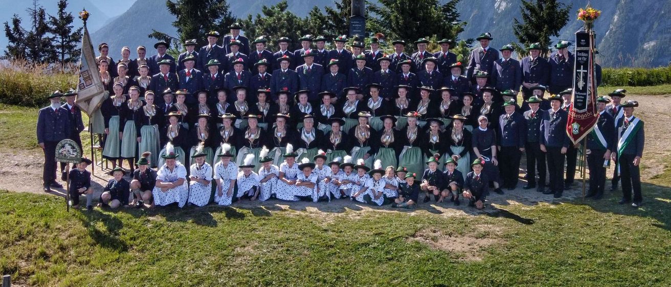 Eine große Gruppe von Menschen in traditioneller Kleidung posiert für ein Foto vor einem Kreuz auf einem Berg.