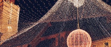 A festive scene with a large illuminated globe hanging from the ceiling, surrounded by sparkling fairy lights. The setting appears to be a night-time outdoor event.