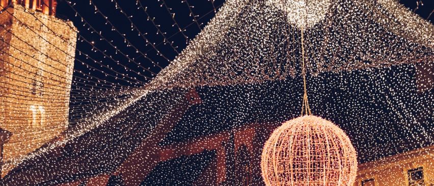 Eine festliche Szene mit einer großen beleuchteten Kugel, die von der Decke hängt, umgeben von funkelnden Lichterketten. Die Umgebung scheint ein nächtliches Outdoor-Event zu sein.