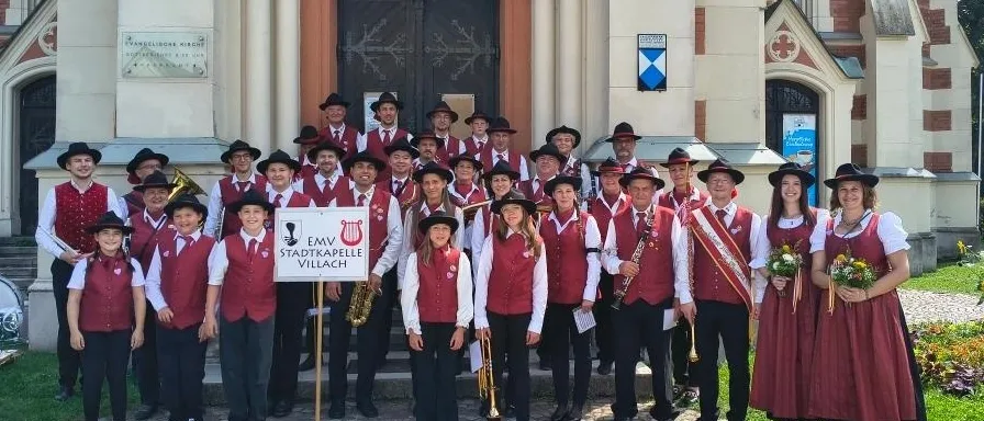 Eine Gruppe von Musikern, die rote Westen und schwarze Hüte tragen, posiert für ein Foto vor einer Kirche.