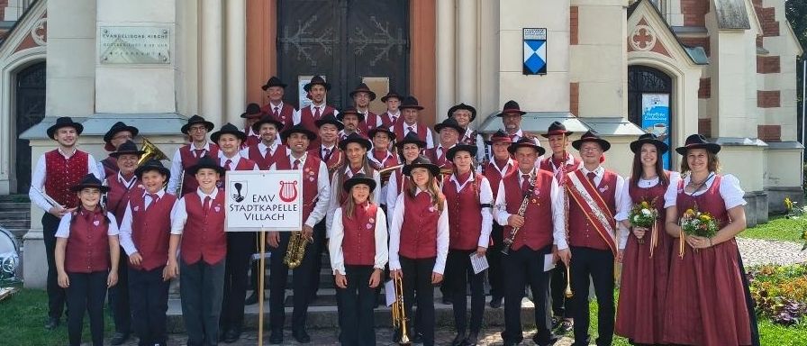 Eine Gruppe von Musikern, die rote Westen und schwarze Hüte tragen, posiert für ein Foto vor einer Kirche.