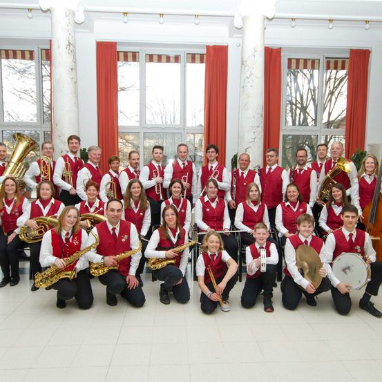 Eine Gruppe von Musikern in roten Westen posiert für ein Foto. Sie halten Musikinstrumente in den Händen.