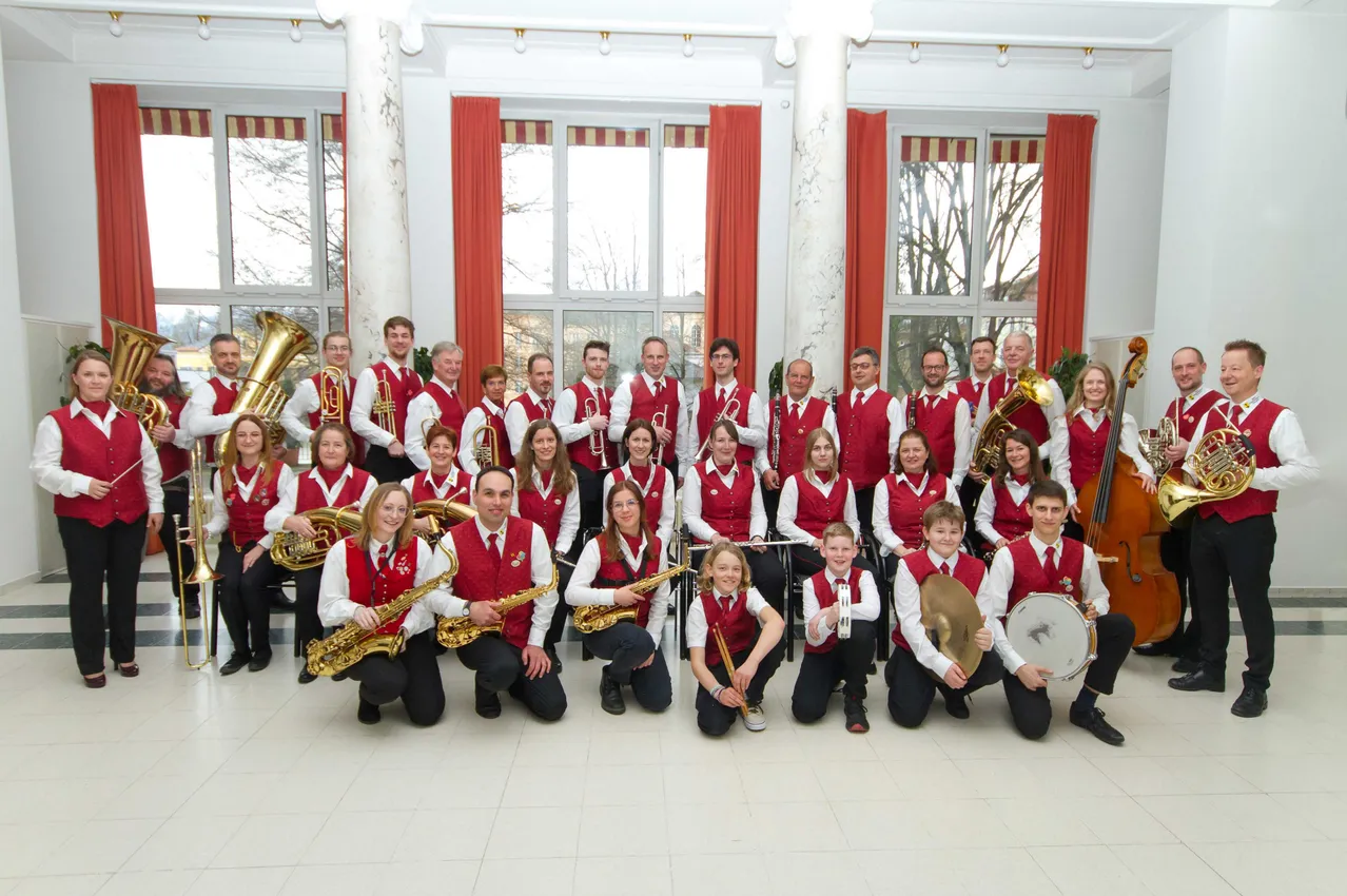 Eine Gruppe von Musikern in roten Westen posiert für ein Foto. Sie halten Musikinstrumente in den Händen.