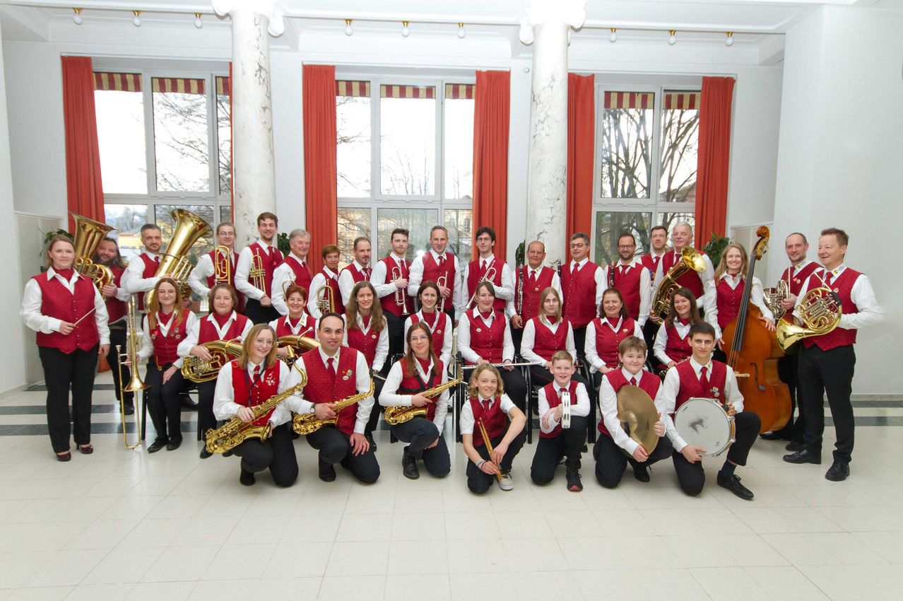 Eine Gruppe von Musikern in roten Westen posiert für ein Foto. Sie halten Musikinstrumente in den Händen.