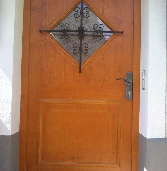 Eine hölzerne Tür mit einem metallischen kreuzförmigen Design und einem silbernen Griff ist an einer weißen Wand montiert.