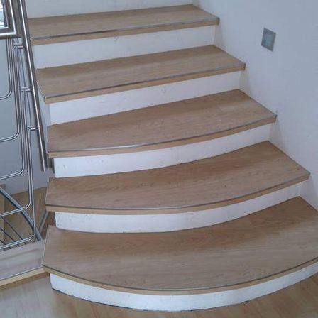 Eine Holztreppe mit mehreren Stufen, weißen Verkleidungen und einem silbernen Handlauf. Der Boden ist aus Holz und die Wand ist weiß.