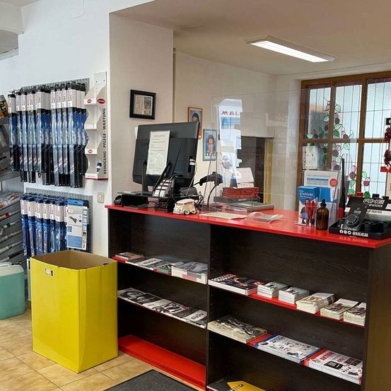 Ein Laden mit einem roten Tresen, Büchern auf Regalen, einem gelben Kasten und einem Monitor. Displays, Rahmen und ein Glasfenster an den Wänden.