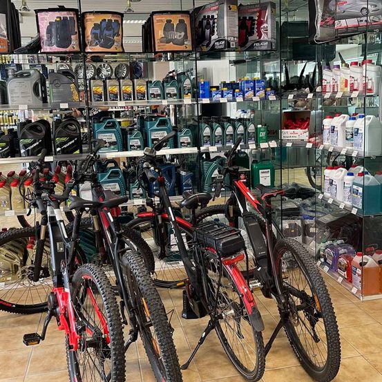 Ein Autoteileladen zeigt verschiedene Fahrräder, Ölflaschen und andere Artikel in Regalen. Drei rote und schwarze Fahrräder sind auf dem Boden geparkt.