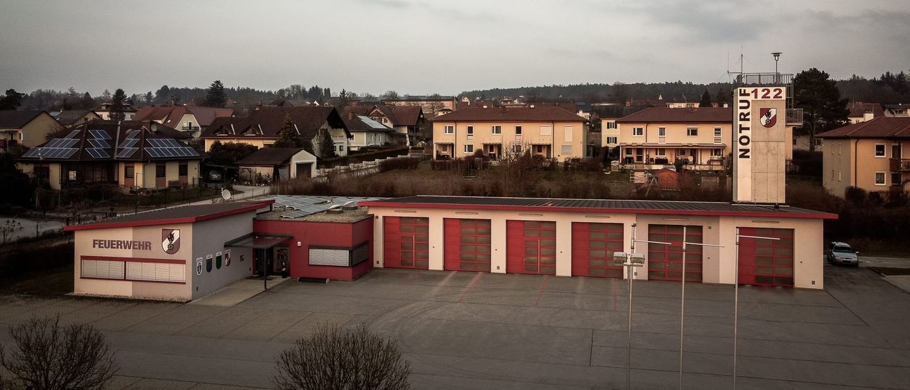 Luftaufnahme einer Nachbarschaft mit roten und gelben Häusern, einem großen Garagengebäude und bewölktem Himmel.