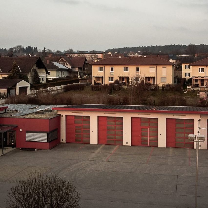 Luftaufnahme einer Nachbarschaft mit roten und gelben Häusern, einem großen Garagengebäude und bewölktem Himmel.