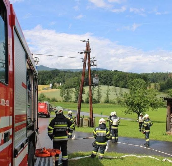Feuerwehrleute stehen in Schutzkleidung auf einer Straße mit einem Feuerwehrauto im Hintergrund.