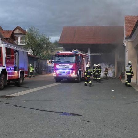 Feuerwehrleute sind am Brandort eines Gebäudes. Zwei Feuerwehrwagen sind geparkt, und Feuerwehrleute in Uniform bereiten sich darauf vor, das Gebäude zu betreten.