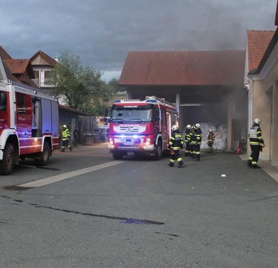 Feuerwehrleute sind am Brandort eines Gebäudes. Zwei Feuerwehrwagen sind geparkt, und Feuerwehrleute in Uniform bereiten sich darauf vor, das Gebäude zu betreten.