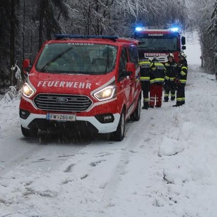 Ein roter Feuerwehrwagen steht auf einer verschneiten Straße. Mehrere Feuerwehrleute stehen auf der Straße. Ein weiterer roter Wagen ist dahinter geparkt.