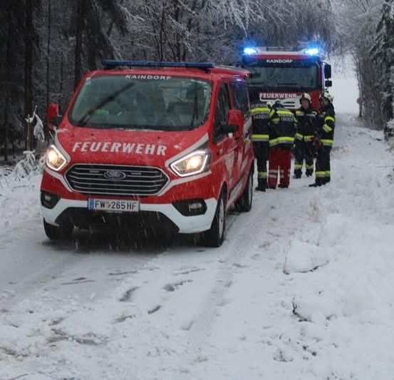 Ein roter Feuerwehrwagen steht auf einer verschneiten Straße. Mehrere Feuerwehrleute stehen auf der Straße. Ein weiterer roter Wagen ist dahinter geparkt.