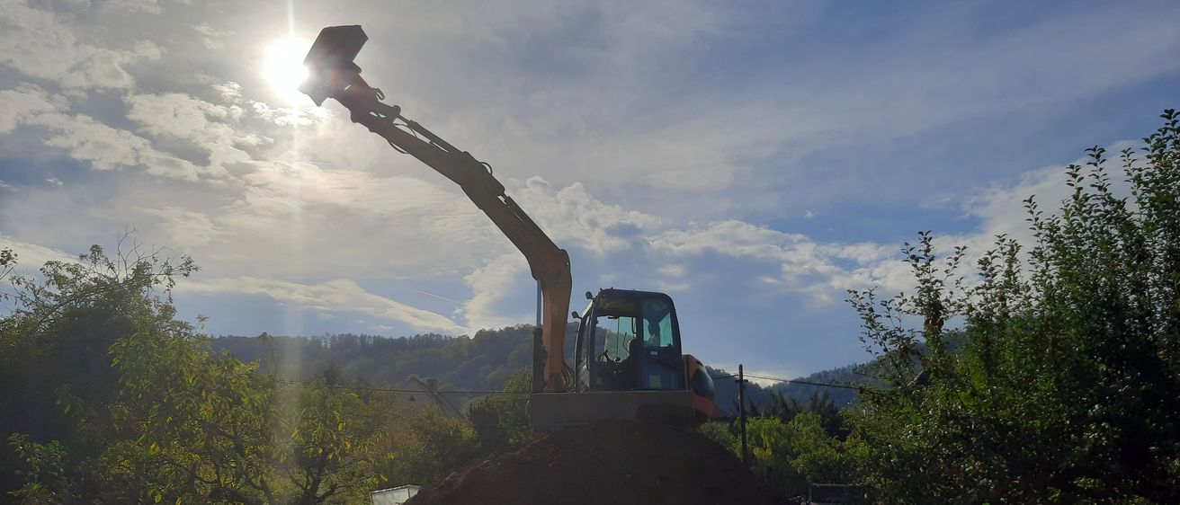 Ein Baufahrzeug steht auf einem Haufen Erde, mit der Sonne, die hell im Hintergrund scheint.