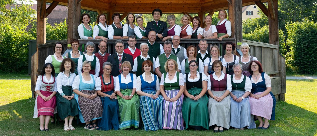 Eine Gruppe von Menschen in traditioneller Kleidung posiert für ein Foto vor einem Pavillon. Die Gruppe besteht aus Männern und Frauen.