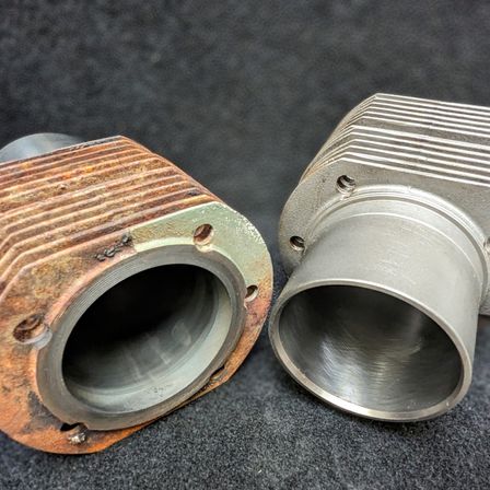 Zwei Motorteile, eines rostig mit einer abgenutzten Oberfläche und das andere poliert und sauber, sind nebeneinander auf einem dunklen Hintergrund ausgestellt.