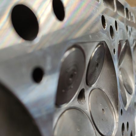Eine Nahaufnahme eines metallischen Motorblocks mit mehreren Löchern, die polierte Oberflächen und komplizierte Designs zeigen. Einige Löcher sind größer als andere, und die Kanten sind scharf.