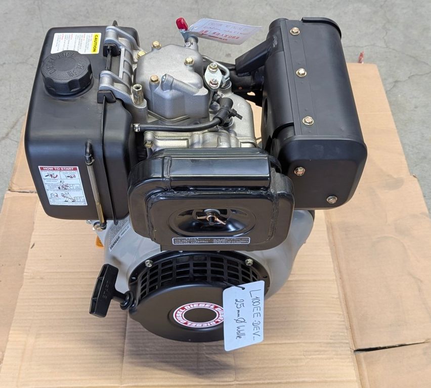 Ein Motor mit einem roten Griff oben ruht auf einer Pappschachtel. Der Motor hat eine schwarze Abdeckung mit silberner Umrandung. Es gibt einen Aufkleber mit Anweisungen, wie der Motor gestartet wird.