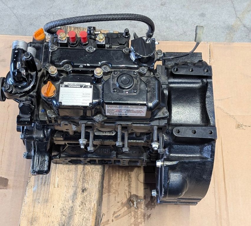 Ein schwarzer Motor liegt auf einer Holzfläche, mit einem weißen Etikett, das den Modellnamen und Informationen anzeigt. Es hat einen angeschlossenen Schlauch und mehrere Schrauben und Schalter.
