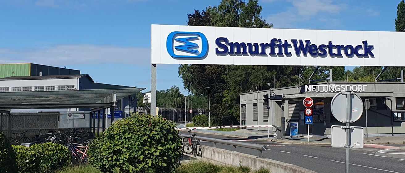 Das Smurfit Westrock-Schild befindet sich auf einem Gebäude mit blauem Himmel und geparkten Autos im Hintergrund.