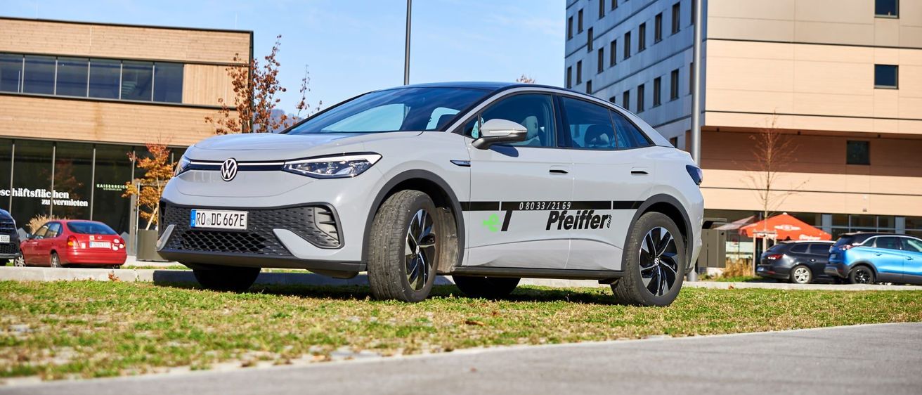 Ein Volkswagen ID.4 Elektrofahrzeug steht vor einem Gebäude mit einem Baum und einer Straßenlampe.