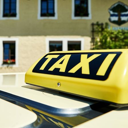 Ein gelbes Taxi-Dachschild ist vor einem gelben Gebäude mit weißen Umrandungen und mehreren Fenstern zu sehen.
