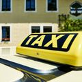 Ein gelbes Taxi-Dachschild ist vor einem gelben Gebäude mit weißen Umrandungen und mehreren Fenstern zu sehen.