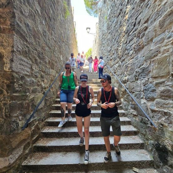 Eine Gruppe von Menschen mit Sonnenbrillen und Rucksäcken klettert über Steinstufen im Freien. Die Stufen sind von Steinmauern umgeben.