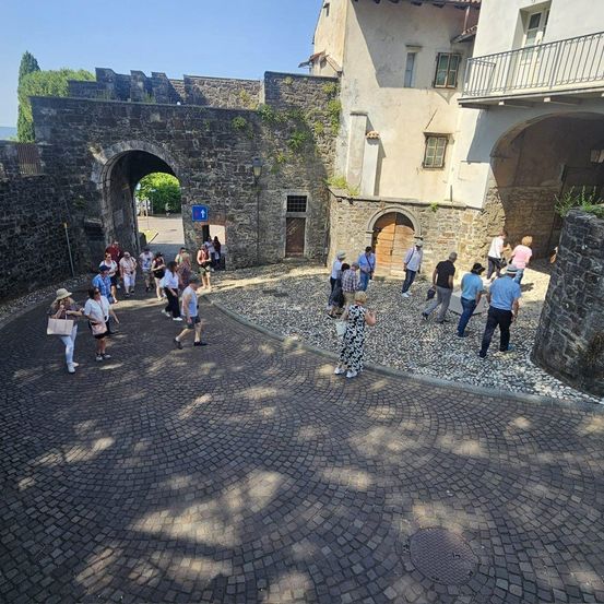 Eine Gruppe von Menschen geht durch einen Bogen in einer historischen Stadt. Gebäude und Kopfsteinpflaster umgeben sie.
