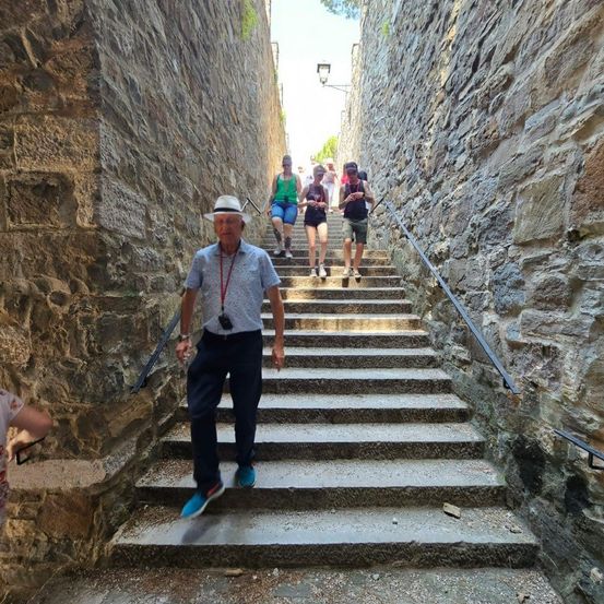 Eine Gruppe von Menschen geht eine Steintreppe hinauf, ein Mann vorne trägt einen Hut und eine Kamera.