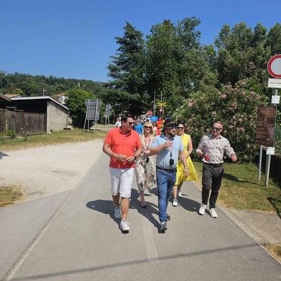 Eine Gruppe von Menschen geht auf einem gepflasterten Weg. Ein Mann trägt ein rotes Shirt, ein anderer ein blaues. Sie scheinen auf einer geführten Tour zu sein.
