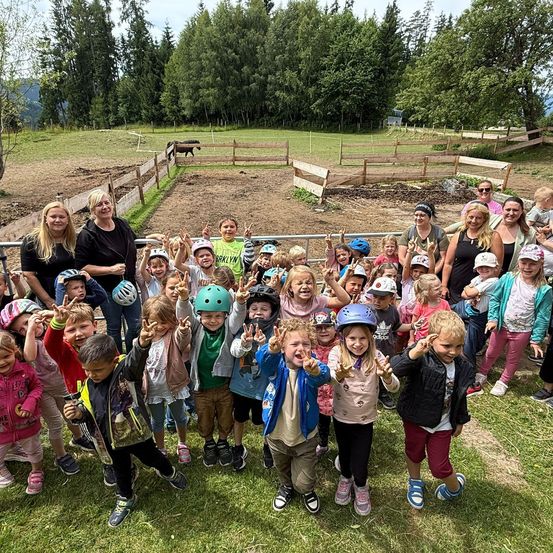 Eine Gruppe von Kindern und Erwachsenen posiert für ein Foto auf einem Bauernhof mit einem Pferd im Hintergrund.