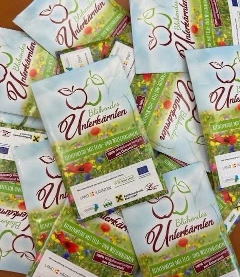 Ein Stapel von Werbebroschüren für 'Bluhende Unterkarnten' mit verschiedenen Blumendesigns auf einer Holzoberfläche. Jede Broschüre hat ein anderes Blumendesign.