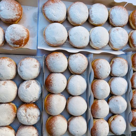 Eine Reihe von Kartons, gefüllt mit frisch gebackenen, puderzuckerbeschichteten Donuts. Jeder Donut ist rund, golden und mit weißem Pulver bestäubt. Die Donuts sind ordentlich in Reihen angeordnet.