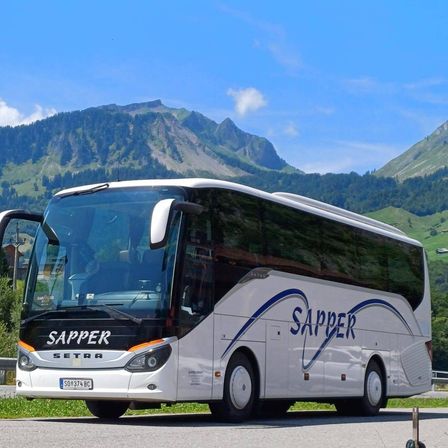 Ein weißer Bus mit dem Wort Sapper an der Seite fährt auf einer Straße mit Bergen im Hintergrund.