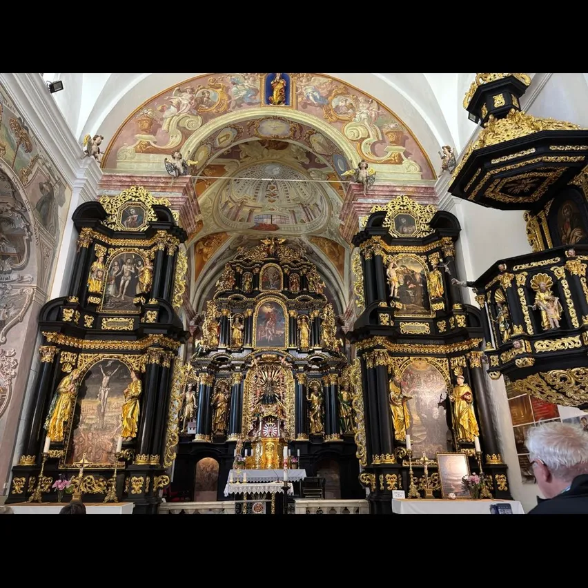 Das Innere einer barocken Kirche mit goldenen Altären, kunstvollen Schnitzereien und religiösen Gemälden. Ein Mann steht im Vordergrund.