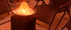 Ein schwach beleuchteter Raum mit mehreren Liegestühlen, weißen Handtüchern und einem zentralen Tisch mit einer brennenden Kerze. Die Wände sind in einem warmen Orangeton gestrichen.