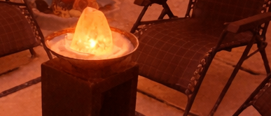 Ein schwach beleuchteter Raum mit mehreren Liegestühlen, weißen Handtüchern und einem zentralen Tisch mit einer brennenden Kerze. Die Wände sind in einem warmen Orangeton gestrichen.