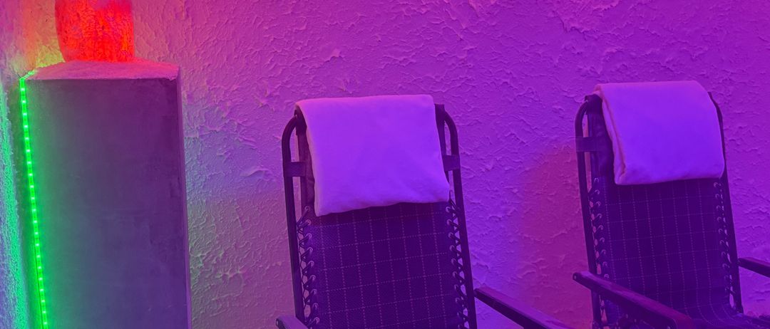 Ein lila Raum mit zwei Stühlen und Kissen. Die Wände sind strukturiert und mit lila und roten Lichtern beleuchtet.