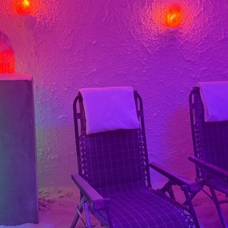 Ein Entspannungsraum im Spa mit zwei Liegestühlen, beleuchtet von roten und lila Lichtern, die eine beruhigende Atmosphäre schaffen.