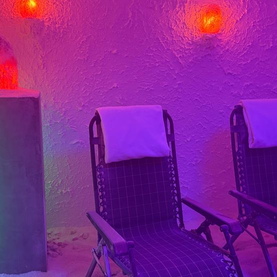 Ein Entspannungsraum im Spa mit zwei Liegestühlen, beleuchtet von roten und lila Lichtern, die eine beruhigende Atmosphäre schaffen.