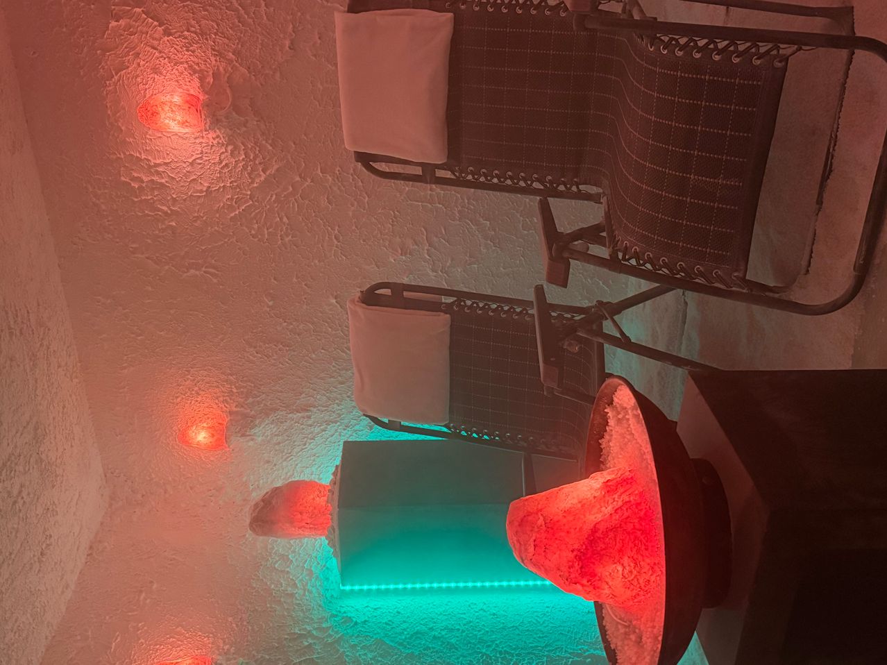 An infrared sauna with two lounge chairs and red and green lighting. A heated salt rock lamp is placed between the chairs.