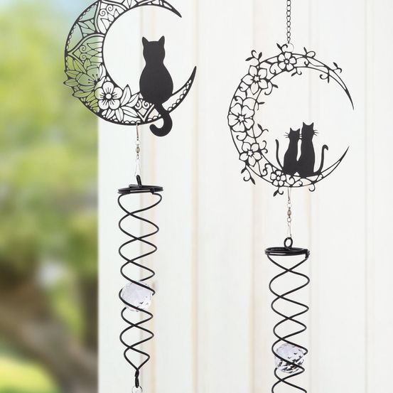 Zwei Windspiele mit schwarzen Katzensilhouetten auf einem Halbmond mit Blumen hängen an Metallketten. Jedes Windspiel hat ein Spiraldesign mit einem Kristallball am unteren Ende.